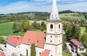 Wehrkirche Krumbach, © Walter Strobl, www.audivision.at Luftaufnahme der Wehrkirche Krumbach in einer ländlichen Umgebung mit grünen Feldern und blauem Himmel.