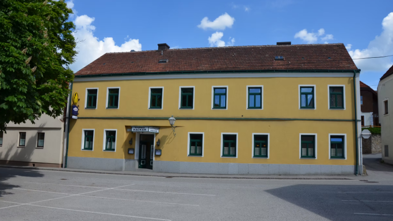 Gasthaus Georg Hacker, © Gasthaus Georg Hacker Gelbes zweistöckiges Gebäude mit grünen Fensterrahmen und einem Schild mit der Aufschrift 'Gasthaus Georg Hacker'.