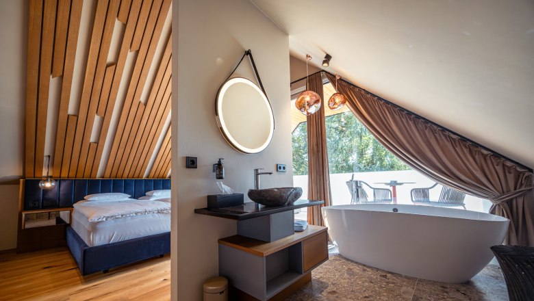 Weindomizil Hagn, © Niederösterreich Werbung / Maximilian Pawlikowsky Modernes Hotelzimmer mit Holzdecke, freistehender Badewanne und Balkon.