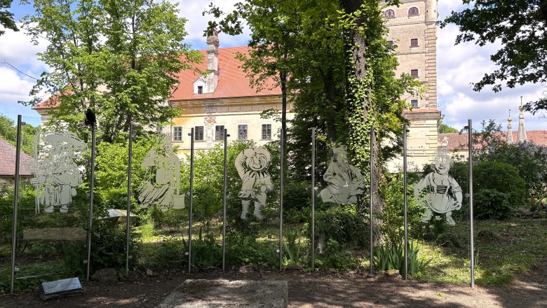 Zwergengarten, © "Natur im Garten" Glasfiguren von Zwergen vor einem historischen Gebäude im Garten.