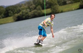 Wakeboarder, © WSC Wakesharks Marbach/Donau Ein Wakeboarder fährt auf einem See, umgeben von grüner Landschaft.