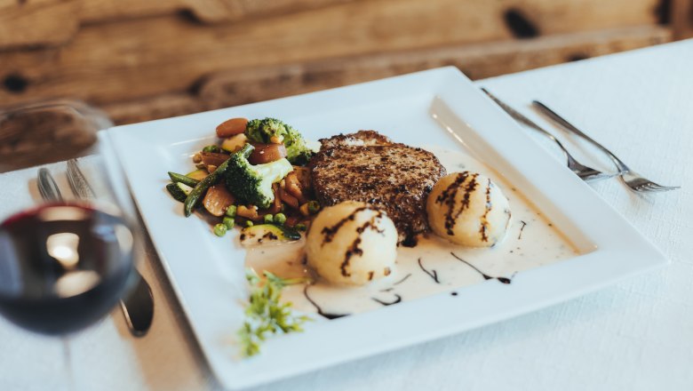 Riesling Kotelett, © Niederösterreich Werbung/David Schreiber Ein Teller mit einem Kotelett, Gemüse und Knödel, garniert mit Soße und Balsamico, auf einem weißen Tisch.