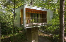 Haus am Fundament, © Robert Tober Modernes Baumhaus im Wald mit Balkon und Glasfront.