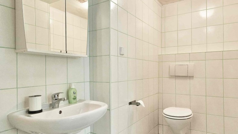 Top 2 - Bad, © VP FeWo OG Modernes Badezimmer mit weißen Fliesen, Waschbecken, Spiegel und Toilette.