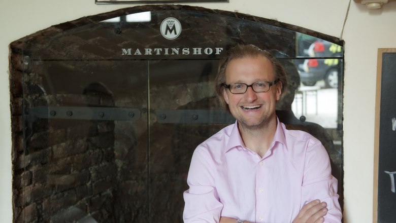 Michael Martin, © Martinshof Ein Mann mit Brille und rosa Hemd steht lächelnd vor einem Schild mit der Aufschrift 'Martinshof'.