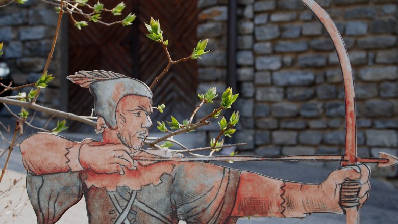 Robin Hood, © Scherz/Kremser Pappfigur von Robin Hood mit Bogen und Pfeil vor einer Steinmauer.