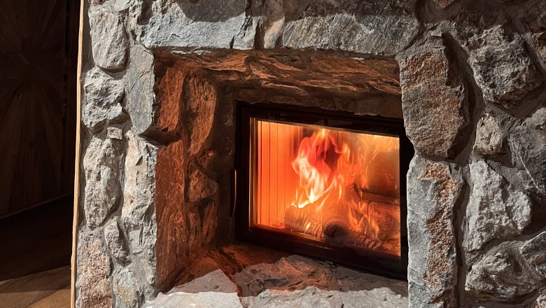Kamin, © RaxChalet Ein brennender Kamin in einer Steinwand eingebaut.