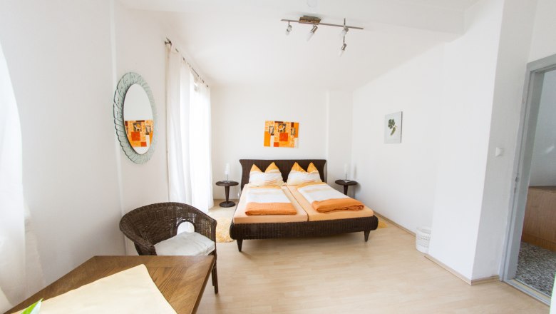 Gästezimmer Winzerhof Lackinger, © Kastner New Media Helles Gästezimmer mit Doppelbett, Rattanmöbeln und Wanddekoration.