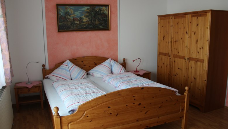 Mehrbettzimmer, © Karl Buchner Ein Schlafzimmer mit einem Doppelbett, zwei Nachttischen, einem Kleiderschrank und einem Gemälde an der Wand.