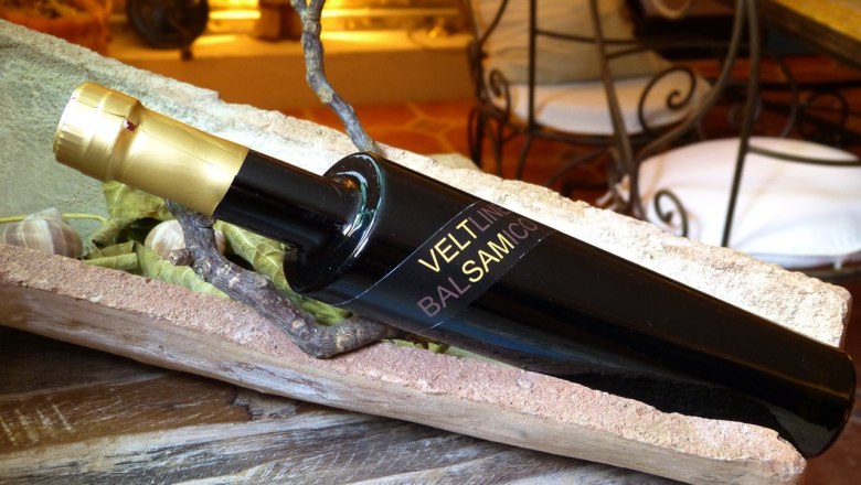 Veltsam Essigflasche, © Familie Mayer Eine schwarze Essigflasche mit goldener Kappe liegt in einer rustikalen Holzschale.