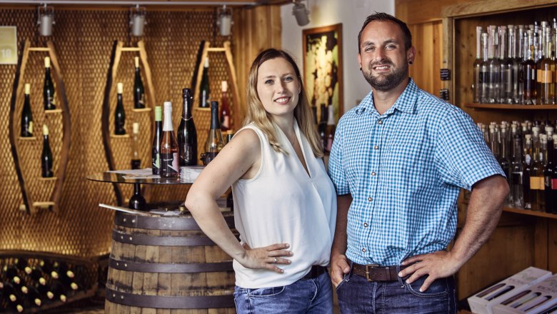 Ab-Hof-Laden Muthenthaler, © Florian Schulte Zwei Personen stehen in einem Ab-Hof-Laden mit Weinflaschen im Hintergrund.