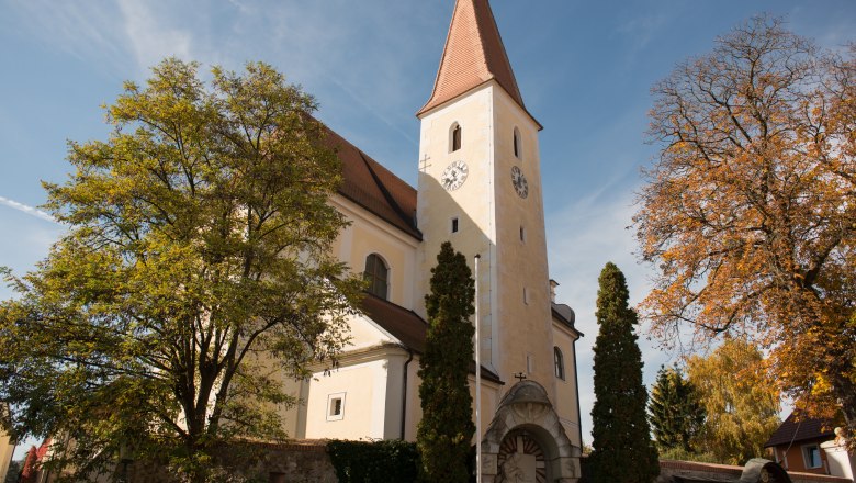 Kirche, © stixenberger Kirche mit Turm und Uhr, umgeben von Bäumen im Herbst.