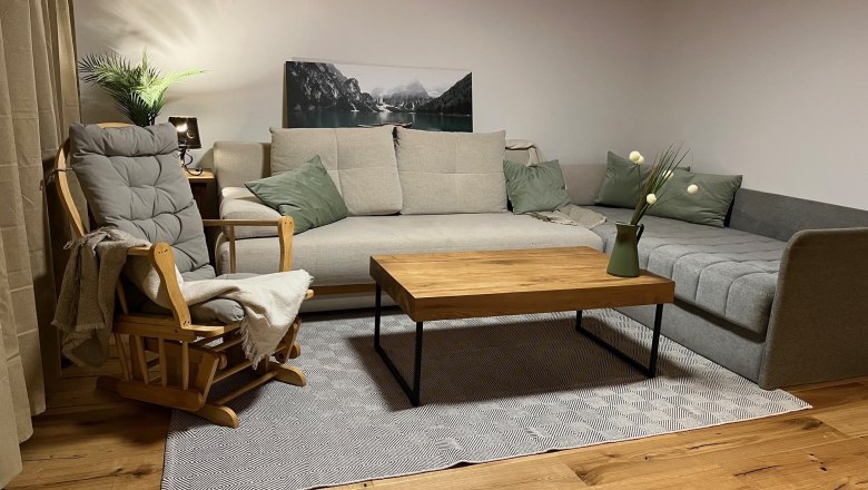 Wohnzimmer- Sitzecke, © Anita Gallei Gemütliche Sitzecke mit grauem Sofa, Holzstuhl, Holztisch und Dekoration in einem Wohnzimmer.