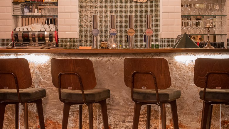 Bar, © Schlossschenke Innenansicht einer stilvollen Bar mit Holzstühlen und beleuchtetem Tresen.