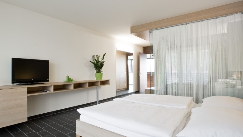 Sauvignon Zimmer, © Rosenberger Modernes Hotelzimmer mit Doppelbett, Fernseher und Pflanzen.