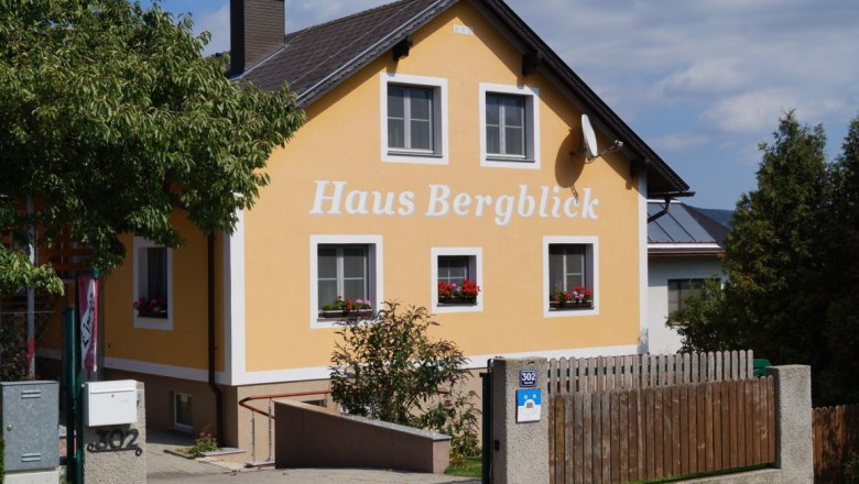 Hausansicht, © Stern Gelbes Haus mit der Aufschrift 'Haus Bergblick', umgeben von Bäumen und einem Holzzaun.
