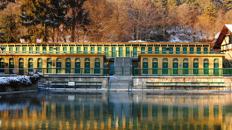 Fischauer Thermalbad - nach der Sauna in das erfrischende Thermalwasser, © Marktgemeinde Bad Fischau-Brunn Historisches Thermalbad mit gelben und grünen Kabinen, umgeben von Bäumen im Winter.