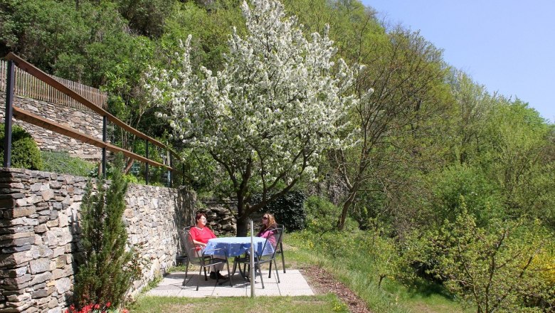 Garten vor der Ferienwohnung Bergkirchner, © Bergkirchner Zwei Personen sitzen an einem Tisch im Garten unter einem blühenden Baum.