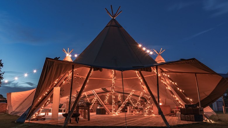 Tipi Beispiel für eine Veranstaltung, © Szilagyi Ein beleuchtetes Tipi-Zelt bei Nacht, dekoriert mit Lichterketten, für eine Veranstaltung vorbereitet.