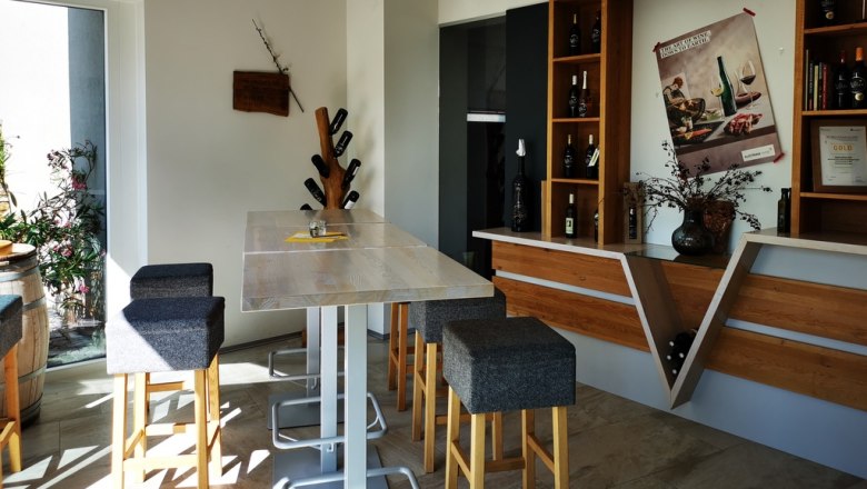 Verkostungsraum, © Weinstraße Weinviertel Moderner Verkostungsraum mit Holztisch, Barhockern und Weinregalen.