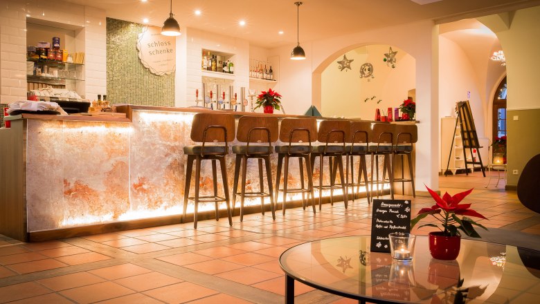 Bar, © Schlossschenke Elegante Bar mit beleuchtetem Tresen und hohen Stühlen, dekoriert mit Weihnachtssternen.