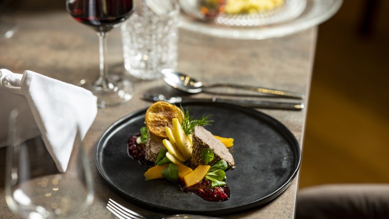 Geflügelleber Pastete, © Niederösterreich Werbung/Michael Reidinger Gourmetgericht auf schwarzem Teller mit Rotwein im Hintergrund.
