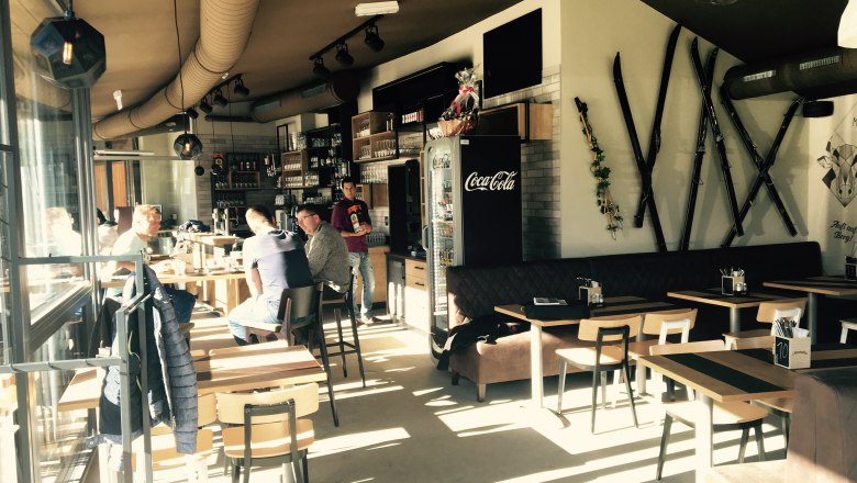 Der Treffpunkt für einen ereignisreichen Tag in der Wexl Arena, © Familienarena Bucklige Welt-Wechselland GmbH Innenansicht eines Cafés mit Holzmöbeln und Skiern an der Wand.