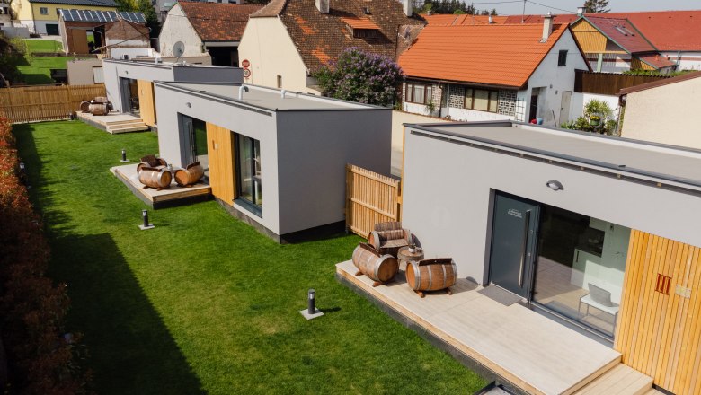 Ipsmiller Appartements, © Michael Reidinger Moderne Appartements mit Holzfass-Dekoration auf grüner Wiese.