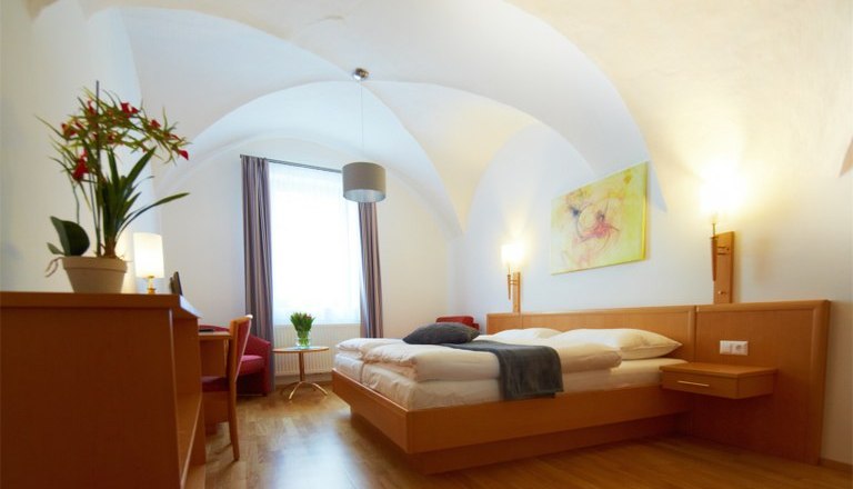Zimmer 2, © Rathauskeller Melk Helles Hotelzimmer mit Doppelbett, Schreibtisch, Pflanzen und Kunstwerk an der Wand.