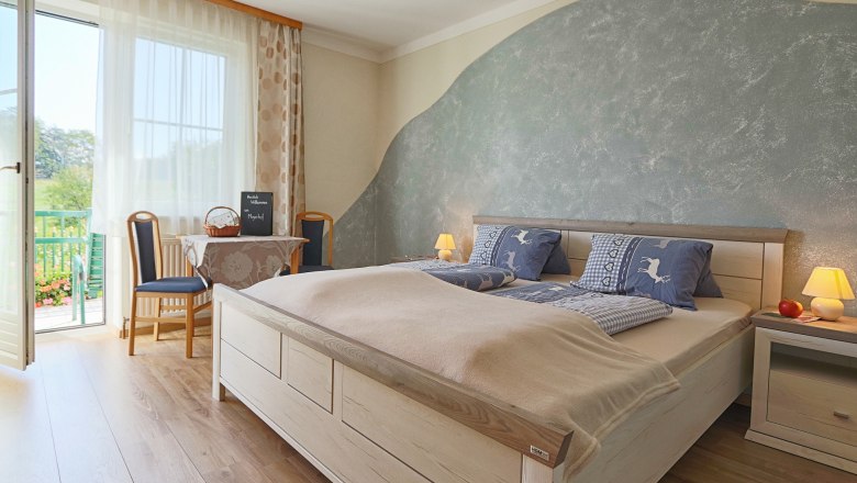 Schlafraum am Mayerhof, © Fam. Mayer Gemütliches Schlafzimmer mit Doppelbett, blauer Bettwäsche, Tisch mit Stühlen und Balkonzugang. Helle, einladende Atmosphäre.