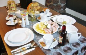 Pension Leichtfried, © Pension Leichtfried Frühstückstisch mit Geschirr, Aufschnitt, Brot, Müsli und Getränken.