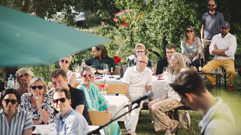 Gastgarten Heuriger Konzert, © Monika Pölzer Menschen sitzen im Freien bei einem Konzert, umgeben von Bäumen und Tischen mit Getränken.