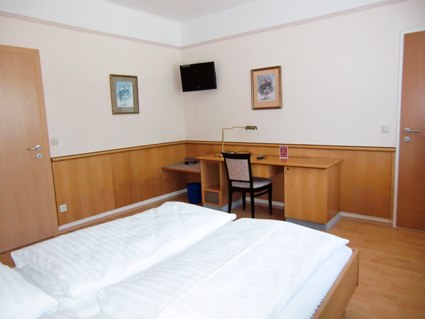 Doppelzimmer, © Weinberger Ein Hotelzimmer mit Doppelbett, Schreibtisch, Stuhl und Wanddekoration.