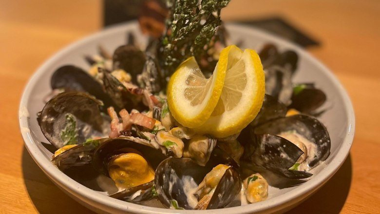 Muscheln im das Freiherr, © Markus Jokesz Ein Teller mit Muscheln, Sahnesoße und Zitronenscheiben auf einem Holztisch.