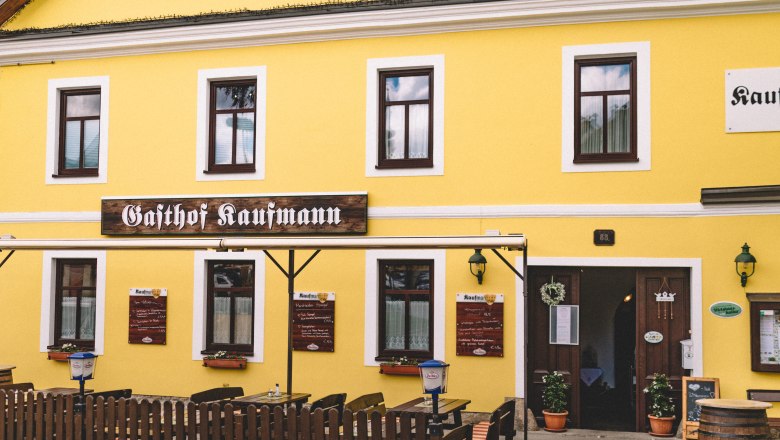 Gasthof in Litschau, © Niederösterreich Werbung/Mara Hohla Gelbes Gebäude mit der Aufschrift 'Gasthof Kaufmann', Holztische und Stühle im Freien.