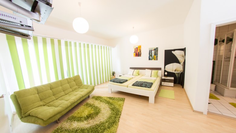 Gästezimmer Winzerhof Lackinger, © Kastner New Media Modernes Gästezimmer mit grünem Sofa, Doppelbett und Bad.