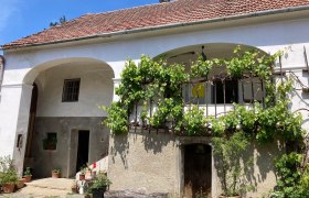 Sonnenblumenhof, © S.Wilhelm Ansicht des alten Hauses mit zwei Bögen und einem Balkon, wo das Geländer mit Wein bepflanzt ist.