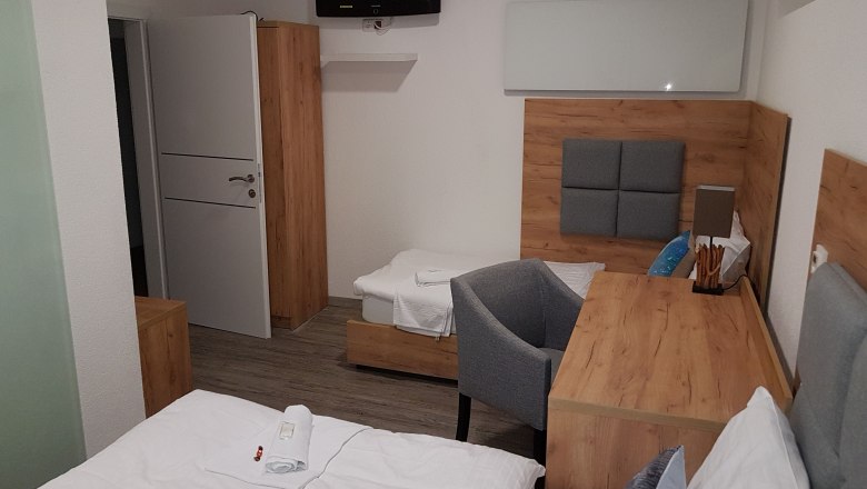 Jedes Zimmer ist anders gestaltet, © Konrad Brandl Hotelzimmer mit Holzmöbeln, zwei Betten, einem Schreibtisch und einem Fernseher an der Wand.