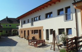 Schmankerl und Gast, © Heiderer Innenhof mit modernen Gebäuden und Holzmöbeln im Freien.