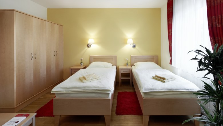 Gästezimmer, © Fam. Dungl Ein Gästezimmer mit zwei Einzelbetten, einem großen Kleiderschrank, roten Vorhängen und einer Pflanze.