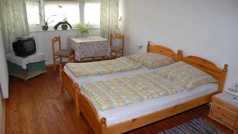 Zimmer im Gästehaus Weiss, © Fam. Weiss Ein gemütliches Gästezimmer mit Doppelbett, kleinem Tisch, zwei Stühlen und einem alten Fernseher.