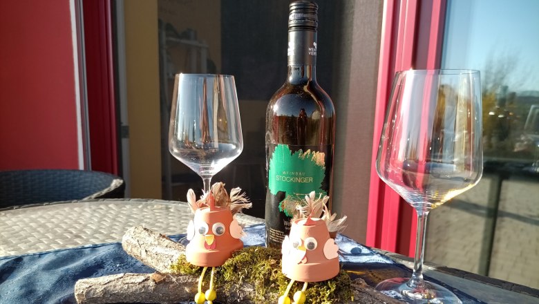 Den Wein genießen, © S. Gritsch-Stockinger Weinflasche mit zwei leeren Gläsern und dekorativen Figuren auf einem Tisch.