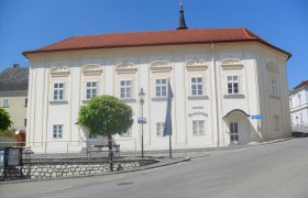 Heimatmuseum Ernstbrunn, © Weinviertel Tourismus Historisches Gebäude mit rotem Dach und weißen Wänden, umgeben von Bäumen und einer Straße.