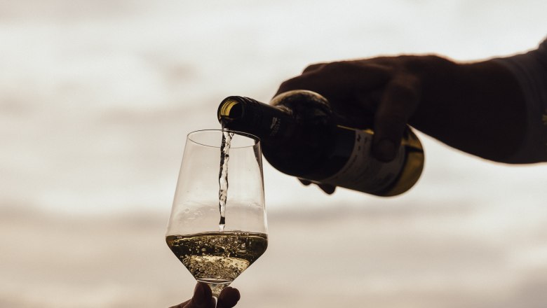 Wein einschenken, © Weinviertel Tourismus / Sophie Menegaldo Wein wird in ein Glas im Freien eingeschenkt, im Hintergrund eine Landschaft.