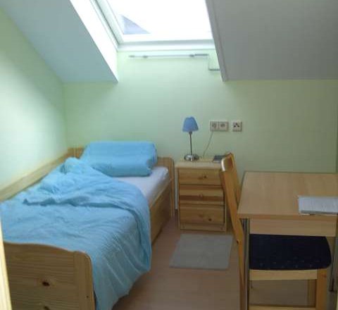 Einzelzimmer, © Reep Ein kleines Einzelzimmer mit Bett, Nachttisch, Schreibtisch und Stuhl unter einem Dachfenster.