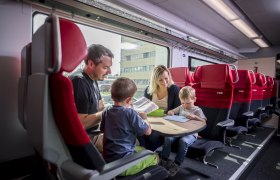 Zug, © Weinviertel Tourismus / Herbst Eine Familie sitzt in einem Zugabteil der ÖBB und beschäftigt sich mit Büchern und Spielen.