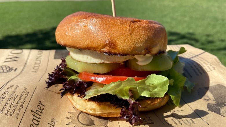 TD-Donaublick Imbiss-Burger, © Donaublick Imbiss Ein Burger mit Salat, Tomaten und Gurken auf einem Tablett im Freien.