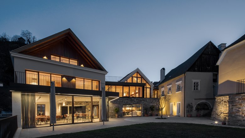 Mauritiushof Weinerlebniswelt Abendstimmung, © Weingut FJ Gritsch Moderne Gebäudes des Mauritiushofes mit großen Fenstern in der Abenddämmerung, beleuchtet von warmem Licht.