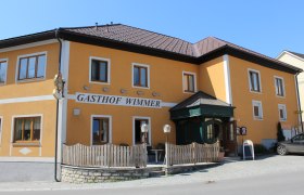 Gasthaus Wimmer, © Fam. Wimmer Gelbes Gebäude mit der Aufschrift 'Gasthof Wimmer', Holzzaun und Eingangstür.