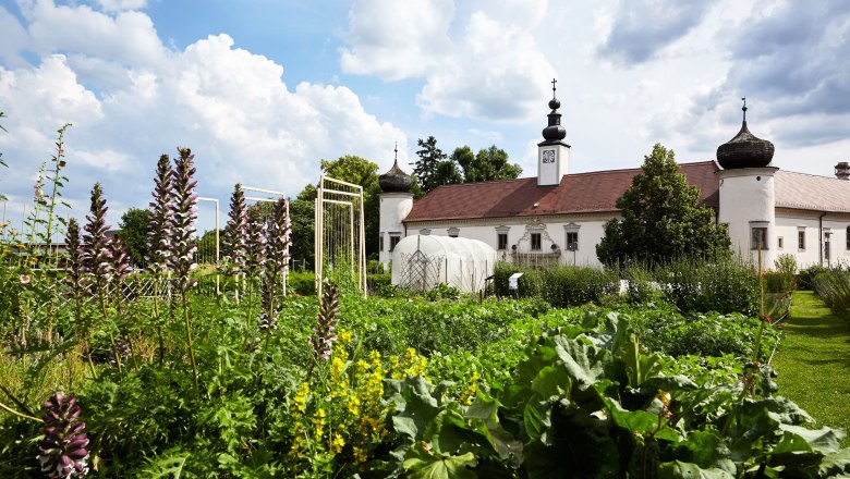 ARCHE NOAH, © ARCHE NOAH Ein Klostergebäude mit Zwiebeltürmen hinter einem üppigen Garten unter blauem Himmel.